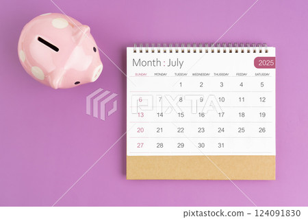 July 2025 desk calendar and pink piggy bank on purple background. 124091830