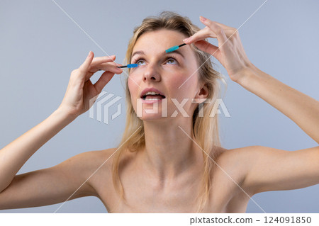 A Glamorous Makeup Application: A Fashionable Young Woman Enhancing Her Eyes with Vibrant Blue Mascara and a Stylish Expression 124091850