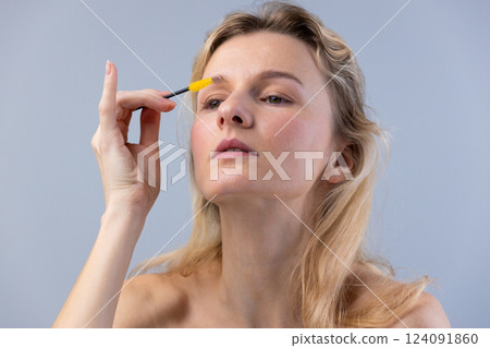 A Woman Focusing on Beauty: Applying Brow Gel for a Perfect Eyebrow Look in a Natural and Calm Setting with Soft Lighting and a Minimalist Background 124091860