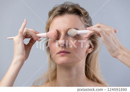 A Young Woman Applying Makeup with Elegant Brushes on a Light Gray Background: The Art of Skincare and Cosmetic Enhancement 124091890