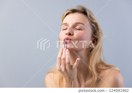 A Beautiful Blonde Woman Embracing Makeup with a Kiss while Holding a Lipstick, Radiating Confidence and Elegance in a Soft Gray Background A Beautiful Blonde Woman Embracing Makeup with a Kiss while Holding a Lipstick, Radiating Confidence and Elegance in a Soft Gray Background 124091902
