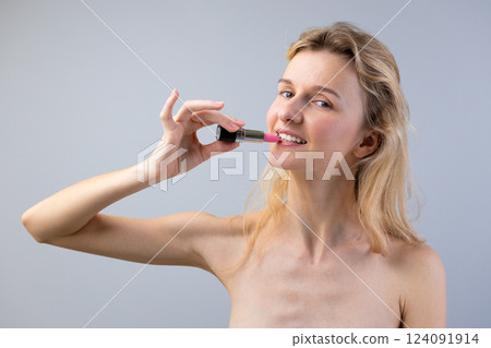 A Playful Moment Featuring a Smiling Woman Holding a Lipstick in Front of Her Lips Against a Soft Gray Background 124091914