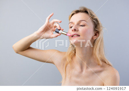 A Captivating Portrait of a Woman Applying Pink Lipstick, Showcasing Natural Beauty and Confidence with Elegant Simplicity Against a Soft Gray Background 124091917