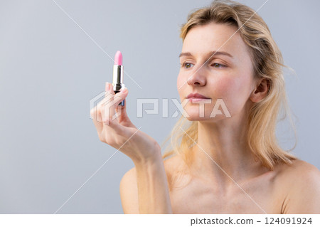 An Elegant Portrait of a Young Woman Holding a Pink Lipstick, Capturing Beauty and Grace in a Minimalist Aesthetic with Soft Lighting and a Serene Expression 124091924