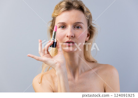 Stylish Beauty Expression: A Close-Up of a Woman Holding a Pink Lipstick Tube Against a Soft Gray Background for Makeup Inspiration and Style 124091925