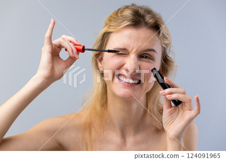 A Smiling Woman Applying Mascara with Confidence, Capturing a Fun Moment in Beauty Routine in a Light and Playful Atmosphere, Perfect for Makeup Lovers and Entrepreneurs A Smiling Woman Applying Mascara with Confidence, Capturing a Fun Moment in Beauty Routine in a Light and Playful Atmosphere, Perfect for Makeup Lovers and Entrepreneurs 124091965