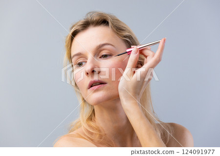 Elegant Woman Applying Eyeliner with Precision Brush for a Flawless Look and Perfect Eye Makeup on a Neutral Background, Emphasizing Beauty and Self-Care Rituals 124091977