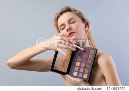 Captivating Beauty: A Woman in Soft Lighting with a Makeup Palette Creating Stunning Looks for Enhanced Elegance and Radiance in Cosmetology and Self-Expression 124092051