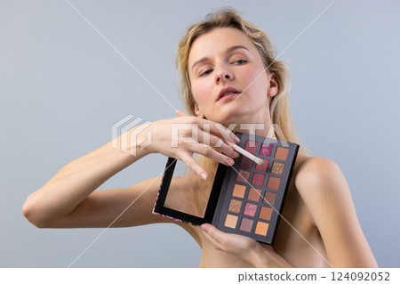 A Stylish Model Showcasing a Vibrant Eyeshadow Palette While Holding a Makeup Brush with a Confident Look Against a Soft Background 124092052