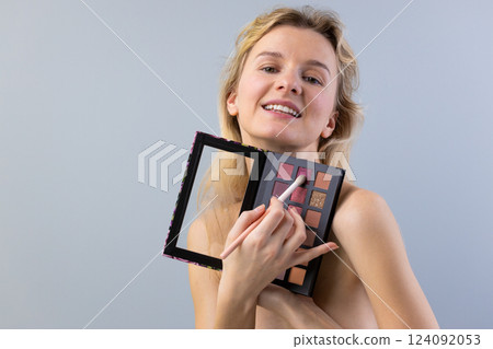 A Young Woman with Flowing Hair Shows Off a Makeup Palette While Smiling, Portraying a Vibrant Sense of Beauty and Confidence in a Stylish Portrait. 124092053
