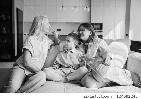 Cozy afternoon in family circle. Joyful children relaxing on couch with their mom. Cute moments of childhood. Cozy spending time with family indoors. Monochrome image. Cozy afternoon in family circle. Joyful children relaxing on couch with their mom. Cute moments of childhood. Cozy spending time with family indoors. Monochrome image. 124092243