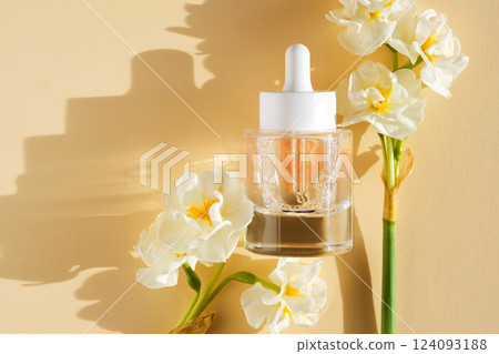 A bottle of luxury serum with petals on a beige background with daffodils. A bottle of luxury serum with petals on a beige background with daffodils. 124093188