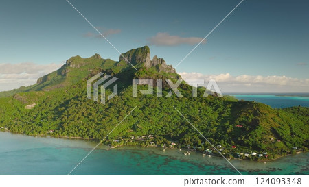 Majestic green mountain rising above Bora Bora turquoise waters, lush landscape under bright blue sky. French Polynesia tropical paradise. Exotic travel vacation getaway. Aerial drone flight zoom in Majestic green mountain rising above Bora Bora turquoise waters, lush landscape under bright blue sky. French Polynesia tropical paradise. Exotic travel vacation getaway. Aerial drone flight zoom in 124093348