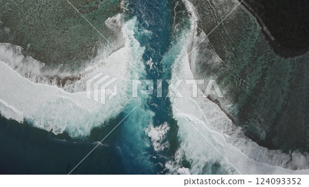 Aerial drone capturing turquoise water flowing between two white foaming waves crashing against dark reefs under a bright sun, creating a stunning tropical seascape 124093352