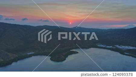 The setting sun casts a warm glow over the rugged landscape of Komodo national park, Indonesia, as seen from an aerial perspective, highlighting the tranquil waters and lush vegetation 124093378