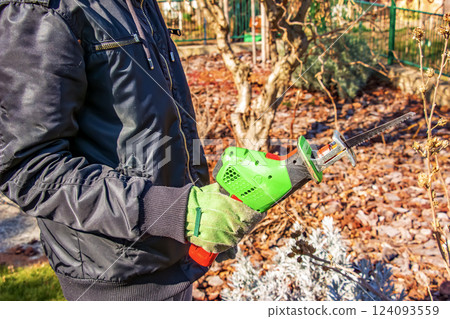 A man holds a mini electric saw for cutting small branches of trees and bushes. 124093559