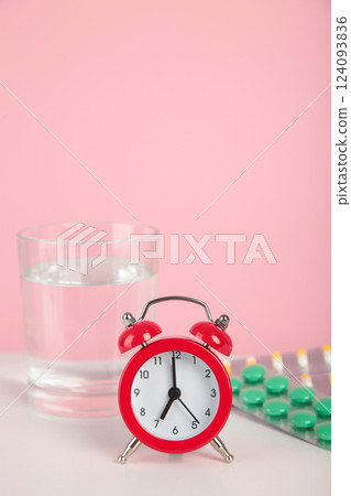 Red alarm clock with glass of water and blister packages of pills on light table background. Red alarm clock with glass of water and blister packages of pills on light table background. 124093836