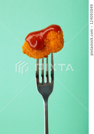 Chicken nugget with ketchup on a fork on mint background. Vertical photo 124093849