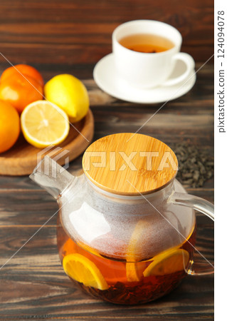 Glass teapot with cup and citrus on brown background. 124094078