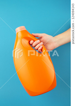 Hand with liquid laundry detergent bottle, cleaning soap for cloth on blue background. Hand with liquid laundry detergent bottle, cleaning soap for cloth on blue background. 124094143