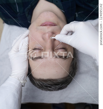 Man undergoing facial cleansing and blackhead removal. Beautician using comedone extractor or uno loop. Professional skin care in a beauty salon Man undergoing facial cleansing and blackhead removal. Beautician using comedone extractor or uno loop. Professional skin care in a beauty salon 124095142