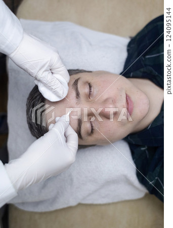 Man undergoing facial cleansing and blackhead removal. Beautician using comedone extractor or uno loop. Professional skin care in a beauty salon Man undergoing facial cleansing and blackhead removal. Beautician using comedone extractor or uno loop. Professional skin care in a beauty salon 124095144
