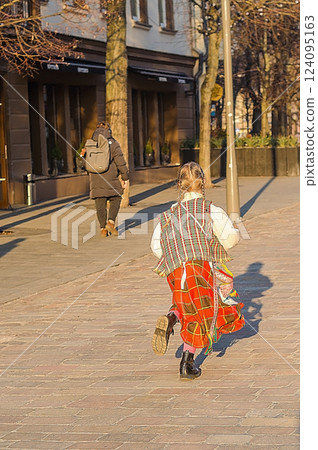 Girl in traditional clothing running on a sunlit cobblestone street in the city. High quality photo 124095163
