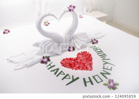 The honeymoon. Two beautiful snow-white swans, as a symbol of love and relationships, decorated with orchid flowers on a white bed for lovers close-up. The Happy Honeymoon inscription is lined with 124095859