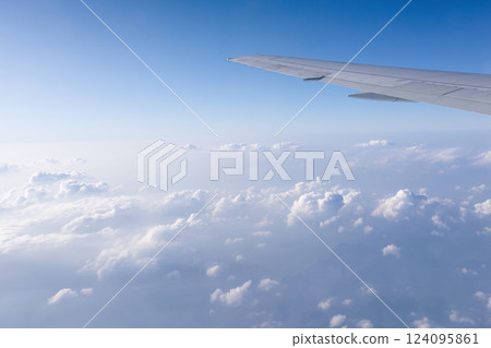 The background of a clear blue sky with white light clouds under the wing of an airliner carrying its passengers on a journey to distant lands. A background for traveling and a free empty space for The background of a clear blue sky with white light clouds under the wing of an airliner carrying its passengers on a journey to distant lands. A background for traveling and a free empty space for 124095861