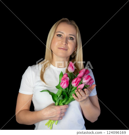 Happy blonde woman in white t-shirt holding bunch of tulips while standing against black background Happy blonde woman in white t-shirt holding bunch of tulips while standing against black background 124096169