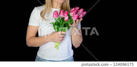 Happy blonde woman in white t-shirt holding bunch of tulips while standing against black background 124096175
