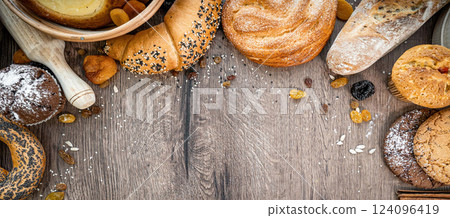 Bakery - various kinds of breadstuff. Bread rolls, baguette, bagel, sweet bun and croissant captured from above (top view, flat lay). wooden rustic background, copy space. Horizontal banner layout. 124096419