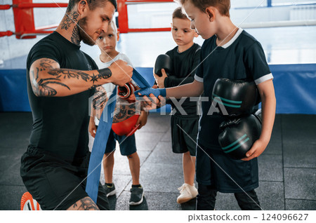 Wearing blue hand wraps. Young tattooed coach teaching the kids boxing techniques Wearing blue hand wraps. Young tattooed coach teaching the kids boxing techniques 124096627