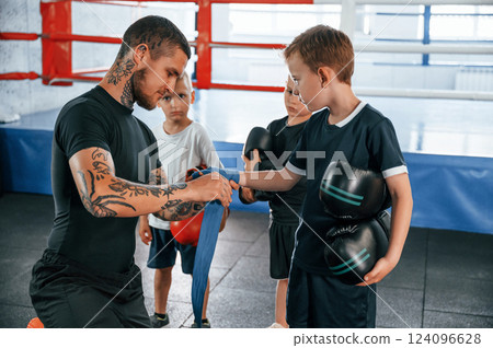 Wearing blue hand wraps. Young tattooed coach teaching the kids boxing techniques Wearing blue hand wraps. Young tattooed coach teaching the kids boxing techniques 124096628