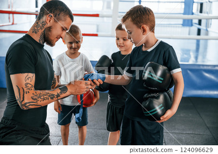 Preparing for the sparring. Young tattooed coach teaching the kids boxing techniques Preparing for the sparring. Young tattooed coach teaching the kids boxing techniques 124096629