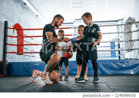 Preparing for the sparring. Young tattooed coach teaching the kids boxing techniques Preparing for the sparring. Young tattooed coach teaching the kids boxing techniques 124096630