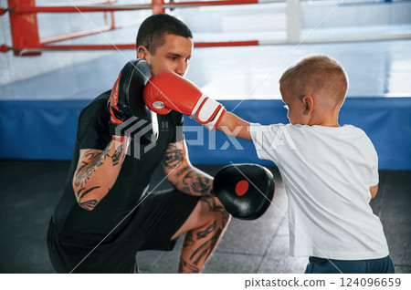 Standing and practicing the punches. Coach is teaching the boy box techniques indoors Standing and practicing the punches. Coach is teaching the boy box techniques indoors 124096659