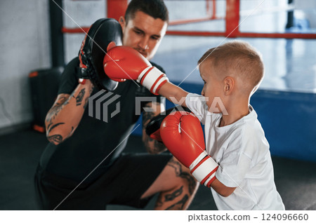 Learning process. Punching the hand. Coach is teaching the boy box techniques indoors Learning process. Punching the hand. Coach is teaching the boy box techniques indoors 124096660