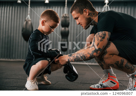 Man is helping kid with learning and practicing. Coach is teaching the boy box techniques indoors Man is helping kid with learning and practicing. Coach is teaching the boy box techniques indoors 124096807