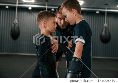 Pre fight preparing. Looking at each other. Young tattooed coach teaching the kids boxing techniques 124096819