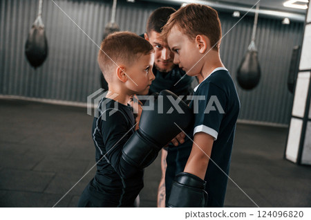 Pre fight preparing. Looking at each other. Young tattooed coach teaching the kids boxing techniques 124096820