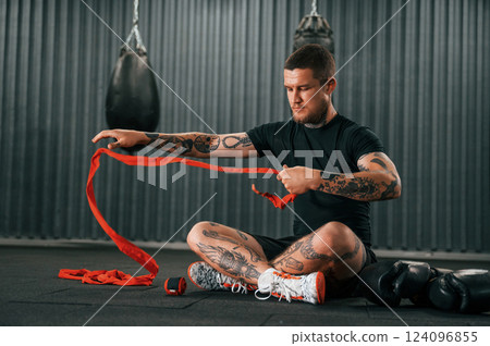 Wearing hand wraps. Young tattooed man is practicing boxing indoors in the gym Wearing hand wraps. Young tattooed man is practicing boxing indoors in the gym 124096855