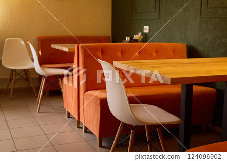 Orange booths and white chairs fill a contemporary dining area. The warm atmosphere is enhanced by inviting wooden tables and stylish decor, perfect for casual gatherings 124096902