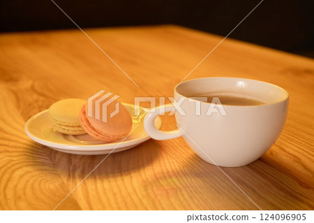 Delicate macarons in soft colors sit on a plate beside a steaming cup of tea on a polished wood table, creating a cozy atmosphere perfect for relaxation Delicate macarons in soft colors sit on a plate beside a steaming cup of tea on a polished wood table, creating a cozy atmosphere perfect for relaxation 124096905