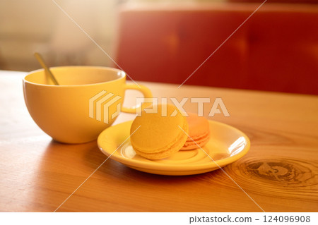 A warm cup of beverage sits beside a small plate with colorful macarons. The soft natural light creates a welcoming atmosphere, perfect for a leisurely break A warm cup of beverage sits beside a small plate with colorful macarons. The soft natural light creates a welcoming atmosphere, perfect for a leisurely break 124096908