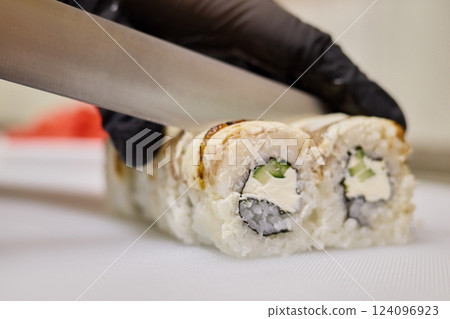 A sushi chef expertly slices a roll filled with fresh ingredients. The kitchen is lively, showcasing the artistry of sushi making during peak lunch time A sushi chef expertly slices a roll filled with fresh ingredients. The kitchen is lively, showcasing the artistry of sushi making during peak lunch time 124096923