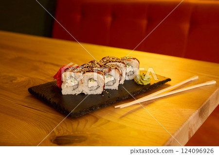 Delicious sushi rolls are arranged neatly on a slate plate, featuring fresh ingredients and garnished with wasabi and pickled ginger, creating an inviting dining experience 124096926