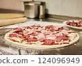 Freshly made pizza dough is spread out on a floured counter, topped with a mix of meats and cheese, ready to be baked in a warm kitchen 124096949