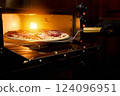 A chef uses a pizza peel to remove a freshly baked pizza topped with meats and cheese from the oven in a lively pizzeria kitchen during nighttime 124096951