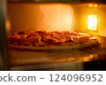 A delicious pizza is baking in an oven, showcasing vibrant toppings like peppers and meat. The warm glow from the oven lights up the kitchen as evening sets in 124096952